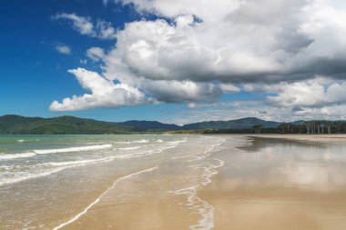 Daintree yağmur ormanlarında beyaz bulutlu mavi gökyüzü altında Queensland, Avustralya 'da tropikal altın kumlu bir sahil. Thornton Sahili güneyde Cape Tribulation Yolu ve doğuda Mercan Denizi ile çevrilidir..
