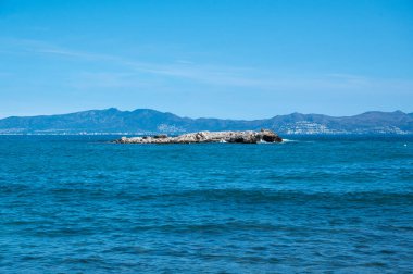 Okyanusun ortasında kayalık bir ada var. Su sakin ve mavidir, ve gökyüzü berrak ve parlaktır. Sahne huzurlu ve sakin, ada izolasyon hissi veriyor.