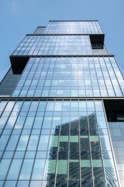 Çağdaş mimari ve şehir gelişimini gösteren, cephesindeki başka bir binayı yansıtan modern cam gökdelenin alçak açılı görüntüsü