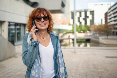 Şehirde yürürken akıllı telefon kullanan mutlu iş kadını, sohbetin ve şehir yaşam tarzının tadını çıkarıyor.