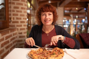 Mutlu kızıl saçlı kadın restoranda oturmuş lezzetli bir pizza yemeye hazırlanıyor.