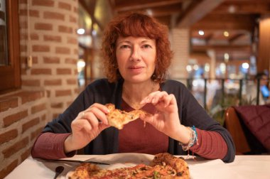 Kızıl saçlı kadın sıcak bir İtalyan restoranında bir dilim lezzetli pizzanın tadını çıkarıyor.