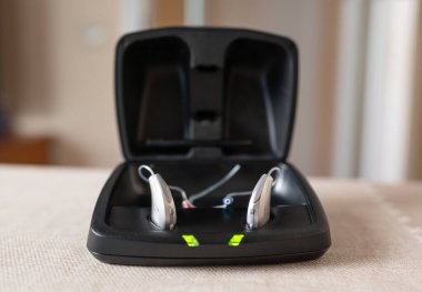 Siyah bir çantada şarj olan bir çift işitme cihazı masa, sağlık ve teknoloji konseptinde