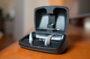 Masada açık siyah bir çantada şarj olan bir çift işitme cihazı