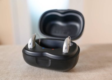 Bir çift işitme cihazı bir masada siyah bir çantada şarj oluyor, işitme ve asistan teknolojisini teşvik ediyor.