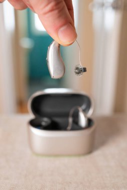 Doktorun işitme cihazı tutarken yakın plan görüntüsü, arka planda şarj ve depolama çantası bulanıklaştırılmış