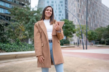 Tablet tutan genç iş kadını modern bir şehirde yürüyor.