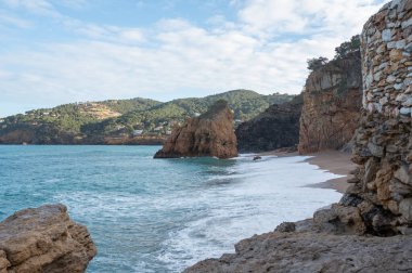 Resimli bir sahilde kaya oluşumları ve uçurumlarla dalgaların kırılma manzarası huzurlu bir kaçış sunuyor.