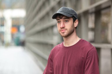 Gündelik kıyafetli genç adam modern bir şehir geçmişine karşı duruyor.