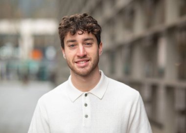 Şık beyaz bir polo tişört giymiş, kendine güvenen, neşeli bir gencin portresi.