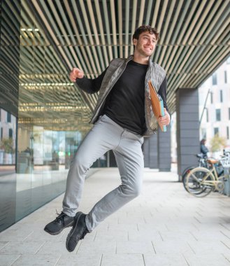 Üniversite koridorunda elinde belgelerle atlayan neşeli öğrenci, neşe ve akademik başarılarını dile getiriyor.