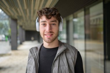 Modern bir şehir ortamında kulaklıkla müzik dinleyen neşeli bir gencin portresi.