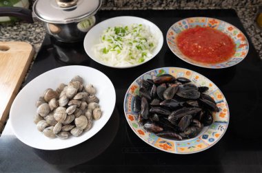 Deniz ürünleri tabağında bulunan midyeler, midyeler, doğranmış domatesler ve soğanlar da dahil olmak üzere bir deniz ürünleri tabağının içeriği seramik bir hob 'un yanında.