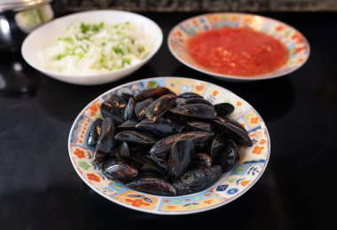 Taze midye, doğranmış soğan ve domates sosu tabaklar üzerinde hazırlanır ve lezzetli bir deniz ürünleri tabağı haline getirilir.