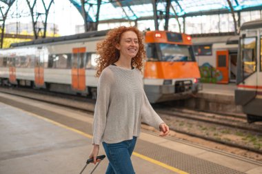 Tren istasyonunda yürüyen kızıl saçlı ve tramvayı olan genç bir kadın.