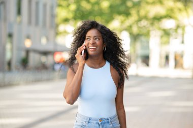 Şehir ortamında sokakta yürürken akıllı telefondan konuşan mutlu iş kadını.