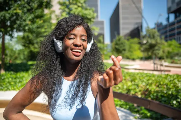 Mutlu Afro-Amerikan kadınları kulaklıklarla müzik dinlemekten hoşlanırlar. Kore 'nin parmaklarını güneşli bir şehir parkında yaparlar.