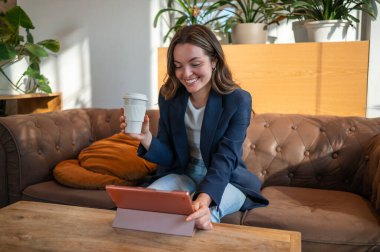 Genç iş kadını, şık bir ofiste dijital tablet üzerinde çalışırken kahve molası veriyor.