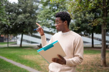 Bina müfettişi elinde bir pano tutarken ve parkta kalemle işaret ederken bir şeyi açıklıyor.