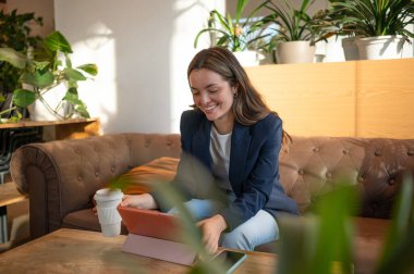 Mutlu yönetici, modern ve parlak bir ofis salonunda tablet kullanıp kahve içiyor.
