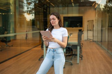 Kendine güvenen iş kadını tablet kullanıyor, modern ofisin dışında duruyor, iş hayatı dengesinin tadını çıkarıyor.
