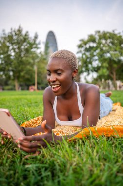 Tablet kullanan genç bir kadın, parkta çimlere uzanmış, dışarıda eğleniyor.