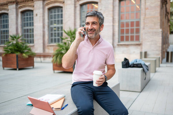 Man talking on phone holding coffee while working remotely in an urban setting