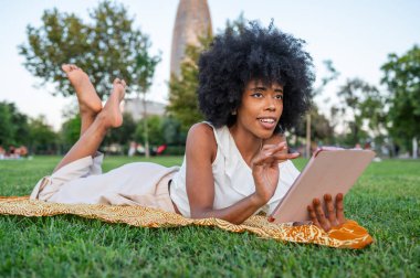 Young woman lying on grass using digital tablet in a park in Barcelona, Spain