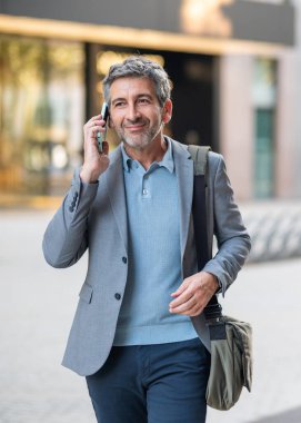 Mature man walking with a bag, smiling during a business phone call