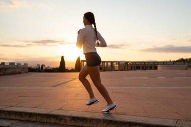 Woman running on an urban platform at sunset, doing a fitness exercise