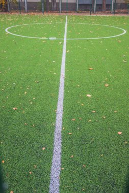 Yeşil futbol sahasında sarı yapraklar. Okulun yakınında yapay yeşil çimenler olan bir futbol sahası. Amatör futbol sahası. Güneşli bir sonbahar günü