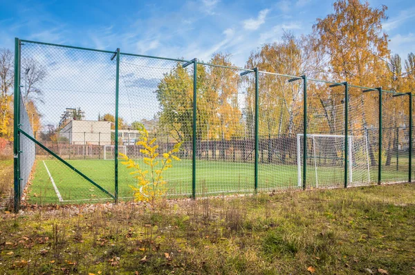 Yeşil futbol sahasında sarı yapraklar. Okulun yakınında yapay yeşil çimenler olan bir futbol sahası. Amatör futbol sahası. Güneşli bir sonbahar günü