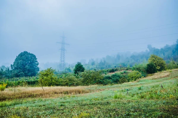 Rural road in a foggy morning on a big mountain. Foggy summer morning in the mountains and a small village. Country road in the mountains.High voltage lines in the fog. Carpathians. Polyana. Ukraine
