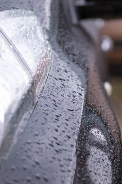 Arabada yağmur damlaları var. Araba parçası yağmur damlalarıyla yakın plan. Yağmur damlalarında siyah bir arabanın kapı kolu ve kapı kolu. Arabadaki yağmur damlaları çok yakındı.