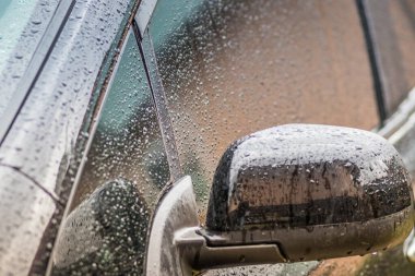 Arabada yağmur damlaları var. Araba parçası yağmur damlalarıyla yakın plan. Kapılar, ayna ve yağmur damlalarında siyah bir arabanın camları. Arabadaki yağmur damlaları çok yakındı.