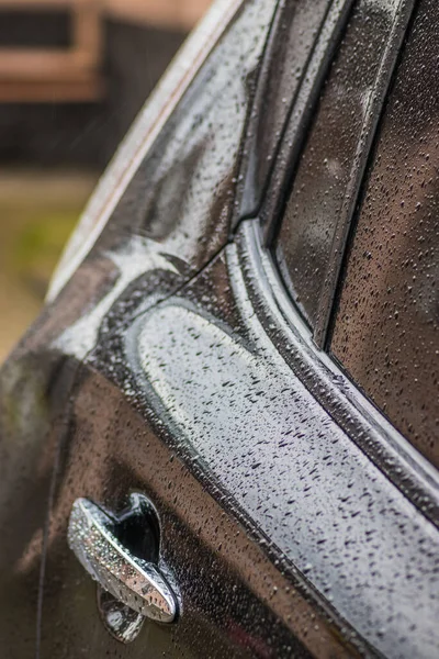 stock image Raindrops on the car. Car element with raindrops close-up. Doors and door handle and glass of a black car in raindrops. Big raindrops on the car very close