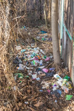 Çitin yanındaki plastik şişeler ve çöpler. Kullanılmış kirli plastik şişeler. Çevre kirliliği. Ekolojik bir sorun. Ahşap çitlerin yanındaki çöplükte.