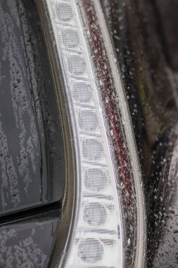 Arabada yağmur damlaları var. Araba parçası yağmur damlalarıyla yakın plan. Arabanın arka camında yağmur damlaları ve çerçevesiz silecek bıçakları var. Arabadaki yağmur damlaları çok yakındı.