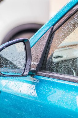 Arabada yağmur damlaları var. Araba parçası yağmur damlalarıyla yakın plan. Kapılar, ayna ve yağmur damlalarında mavi bir arabanın camları. Arabadaki yağmur damlaları çok yakındı.