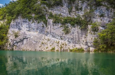 Güzel, berrak mavi Plitvice Gölleri manzarası. Mavi suyu olan göllerin etrafındaki kayalar ve yeşil ağaçlar. Hırvatistan 'daki Plitvice Gölleri Ulusal Parkı nefes kesici bir manzara.