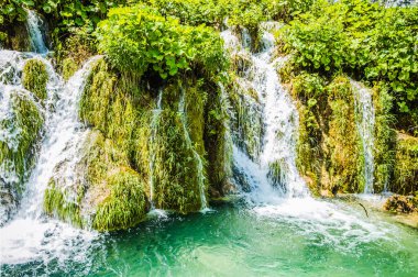 Plitvice Gölleri 'ndeki güzel şelalelerin manzarası. Mavi suyu olan göllerin etrafındaki kayalar ve yeşil ağaçlar. Hırvatistan 'daki Plitvice Gölleri Ulusal Parkı nefes kesici bir manzara.