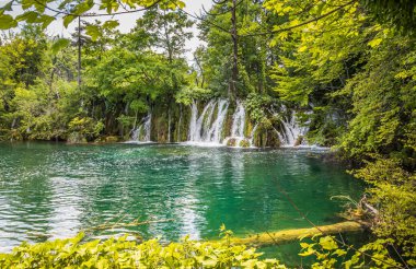 Plitvice Gölleri 'ndeki güzel şelalelerin manzarası. Mavi suyu olan göllerin etrafındaki kayalar ve yeşil ağaçlar. Hırvatistan 'daki Plitvice Gölleri Ulusal Parkı nefes kesici bir manzara.