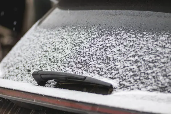 Close-up shot of a car\'s windscreen wiper covered in snow. Fresh snow lies on the car window.