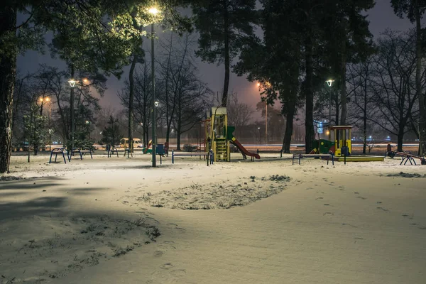 The snowy roads in the night park with lanterns in the winter. Benches in the park during the winter season at night. Illumination of a park road with lanterns at night. Snow on trees. Park Kyoto.Kyiv