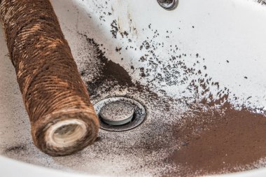 Beyaz bir lavabodaki su filtresinden kirli parçacıklar düşüyor. Temiz ve sağlıklı su için filtreleme sistemi elementleri. Ekoloji ve kirli su