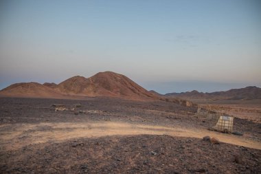 Çöldeki ahşap ahır. Güneş battıktan bir saat sonra çöldeki dağların arkasında Mısır Sandy ön planda, kayalık dağlar arka planda karaya çıkar. Gün batımında gökyüzünde küçük bulutlar.