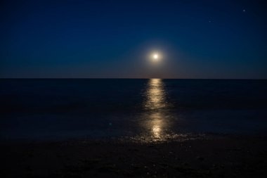Dolunay, okyanus üzerinde gece gökyüzünü aydınlatır. Suya güzel bir parıltı yayar ve dingin bir atmosfer yaratır.