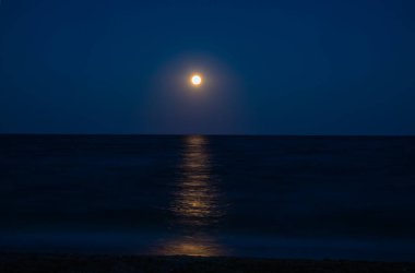 Dolunay, okyanus üzerinde gece gökyüzünü aydınlatır. Suya güzel bir parıltı yayar ve dingin bir atmosfer yaratır.