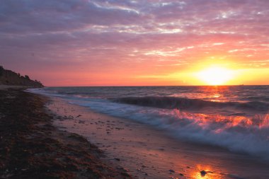 Güneş ufkun altına batarken, onun altın ışığı okyanusu sıcak bir ışıltıyla kaplarken dalgalar ritmik bir şekilde kumlu sahile çarpıyor.