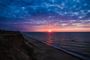 Güneş ufkun altına batarken, onun altın ışığı okyanusu sıcak bir ışıltıyla kaplarken dalgalar ritmik bir şekilde kumlu sahile çarpıyor.